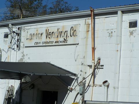 1971 Ford Ranchero - Exterior of a white brick building with a sign indicating it is Lanier Vending. Co., specializing in coin-operated machines.
