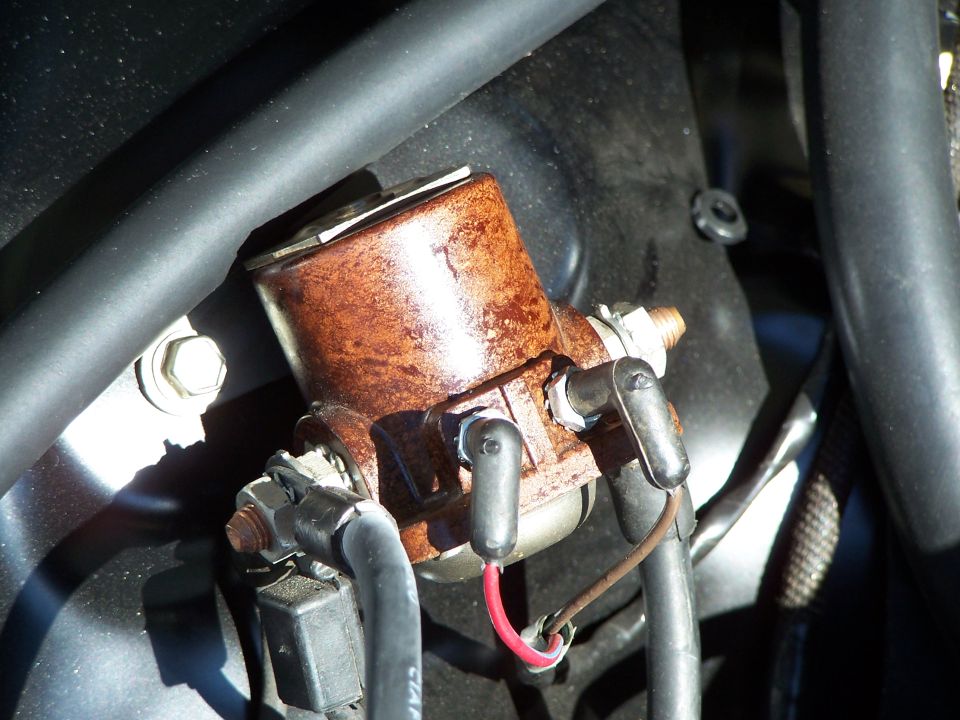 Rusty starter solenoid with black and red wires connected, surrounded by black hoses