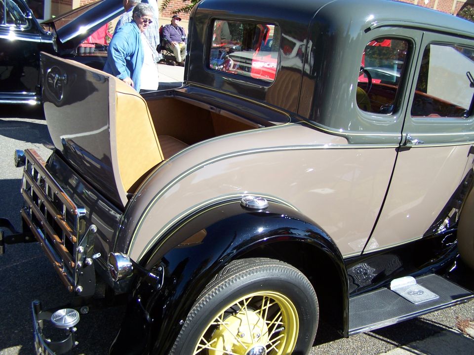 Rear view of a two-tone brown and gray 1930 Ford Model A coupe, showing the open rumble seat and wooden bed rack