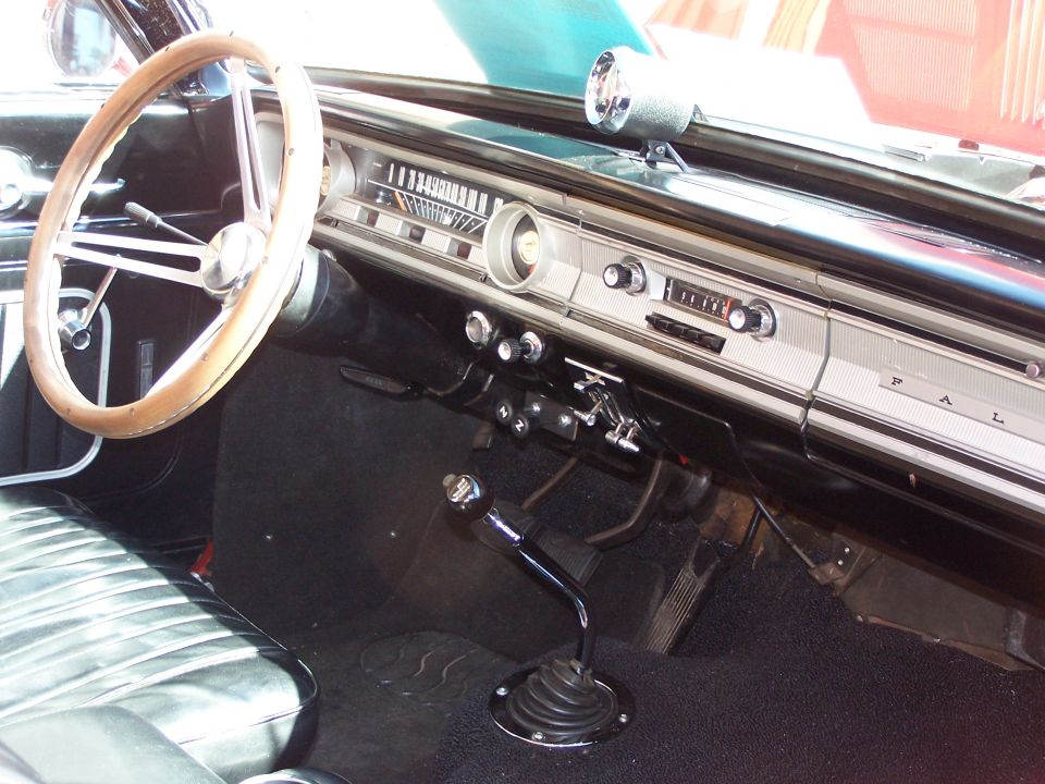 Dashboard and steering wheel of a vintage car, showing the instrument cluster, radio, and shifter