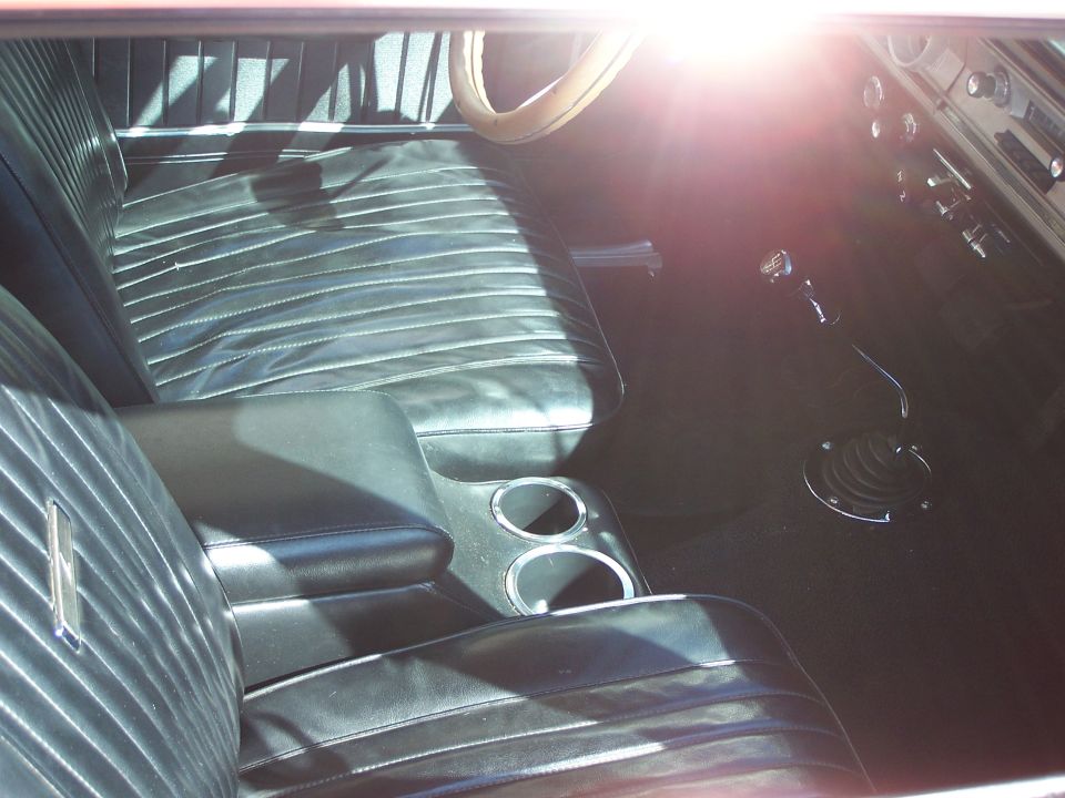 Black vinyl bench seat interior with center console and floor shifter. Sun glare on dashboard