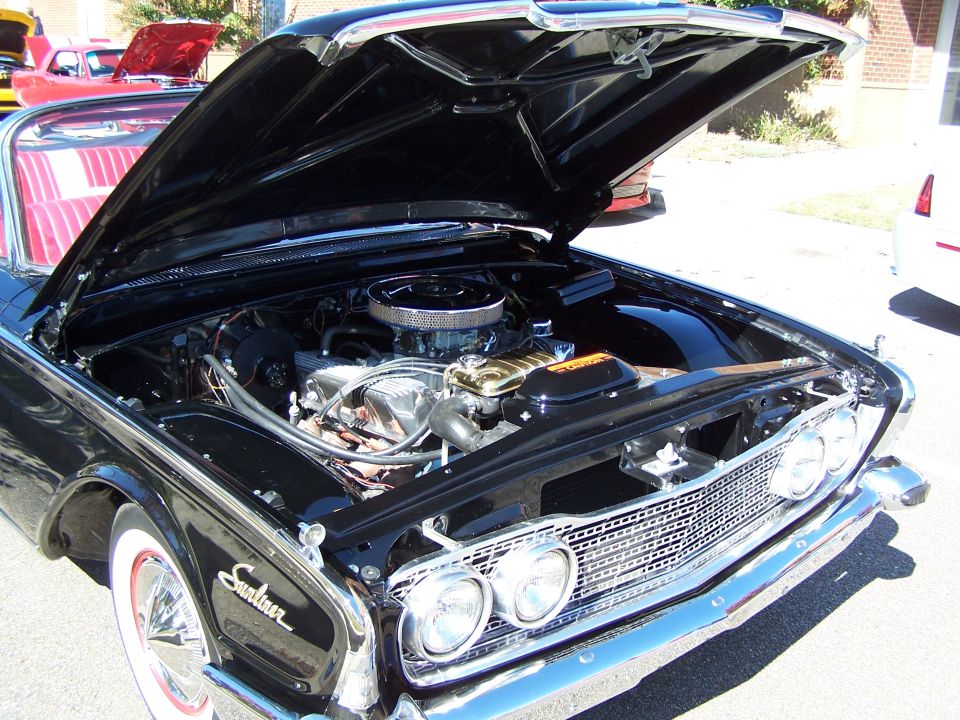 1960 Ford Falcon with hood open showing V8 engine. Red car in background