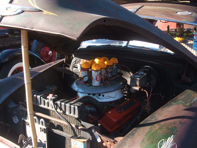 Engine bay with V8, multiple carburetors topped with orange lids, and a bamboo support