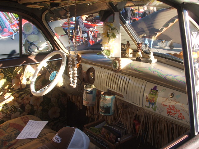 Car interior with floral upholstery, white steering wheel, and dashboard decorated with figurines and cans