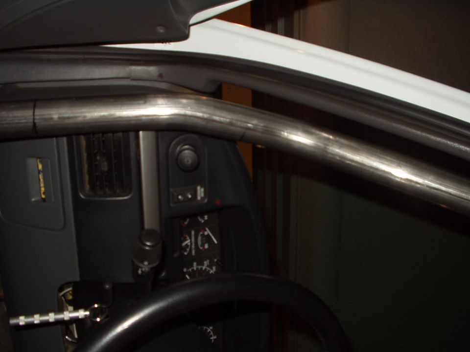Bare metal roll bar along A-pillar with gray dash and switches inside vehicle
