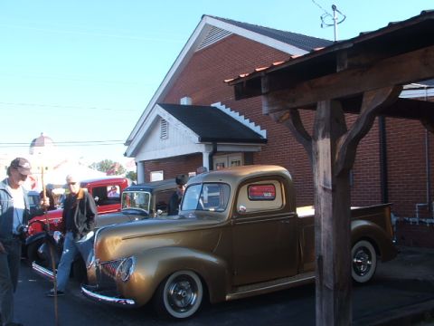 1971 Ford Ranchero - A gold pickup truck is parked next to other vintage vehicles outside a brick building.
