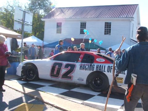 1971 Ford Ranchero - A race car is displayed on a checkered mat in front of a building with people around.