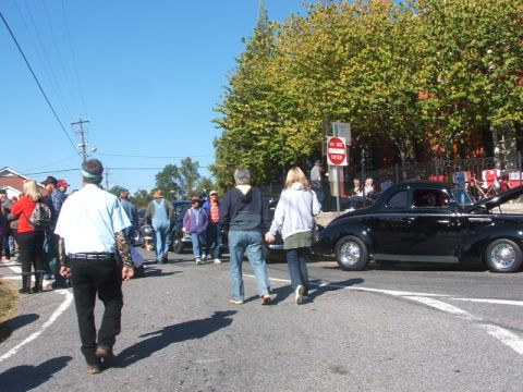1971 Ford Ranchero - A black coupe with its hood open is parked on the street during an outdoor event with people milling around.