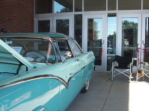 1971 Ford Ranchero - A vintage two-tone turquoise and white coupe with its hood open is parked in front of a building with glass doors.