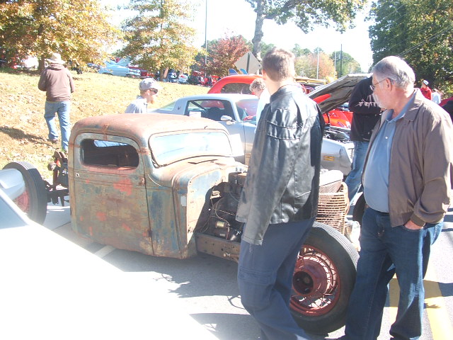 Rusty old pickup truck cab with no hood or fenders, people standing around it