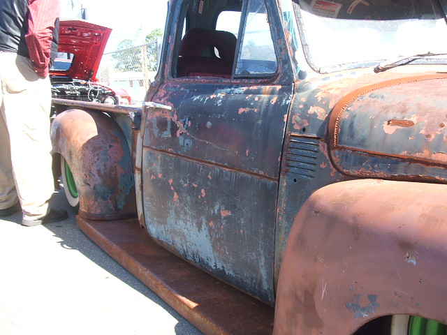 Rusty pickup truck side view, showing peeling paint, rust, and a person standing nearby