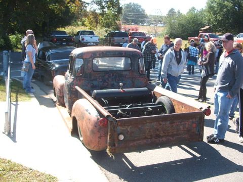 1971 Ford Ranchero - A weathered pickup truck, likely from the 1950s, is displayed with its engine exposed, drawing a crowd of onlookers.