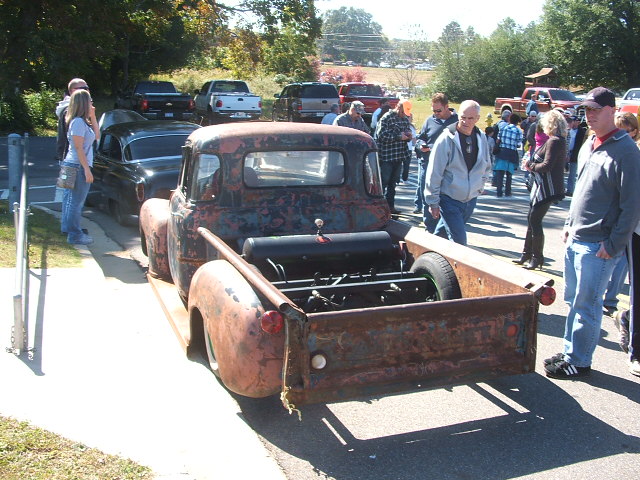 Rusty pickup truck bed with exposed engine and people gathered around