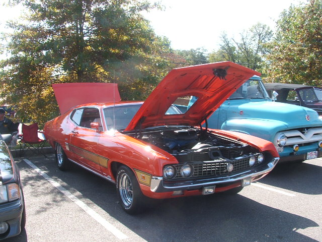 Orange 1970s Ford Ranchero with hood open, parked next to a light blue 1950s Ford truck