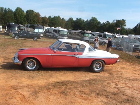 1971 Ford Ranchero - Side view of a red and white Studebaker Hawk coupe at an outdoor event with RVs in the background.