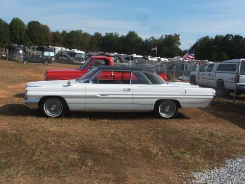 1971 Ford Ranchero - A classic white convertible coupe is parked in a grassy area with several RVs and trucks in the background.