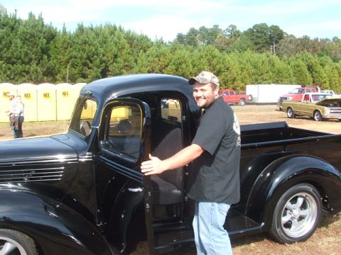 1971 Ford Ranchero - A man stands by a classic black pickup truck with its door open, while other vehicles are visible in the background.