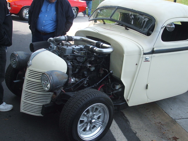 Custom hot rod with large engine and exposed turbocharger. Red car in background