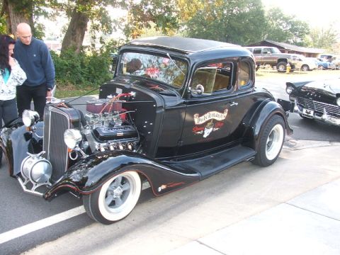 1971 Ford Ranchero - A custom hot rod coupe with a prominent engine is displayed outdoors, with people looking at it.
