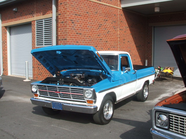 Blue and white pickup truck with hood up, parked next to another truck