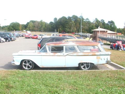 1971 Ford Ranchero - A light blue station wagon with surfboards on its roof rack is parked in a lot, showing signs of rust on its roof.