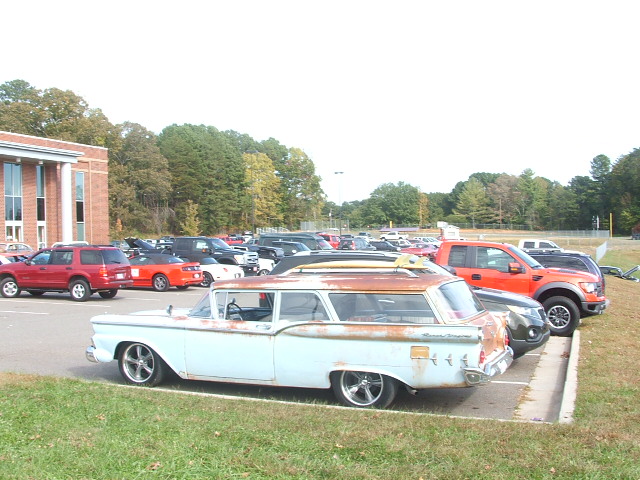 Light blue station wagon with surfboards on roof rack, parked in a lot with other vehicles