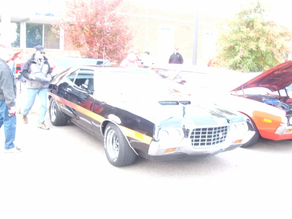 Black Ford Ranchero with orange stripe, parked next to an orange car with hood up