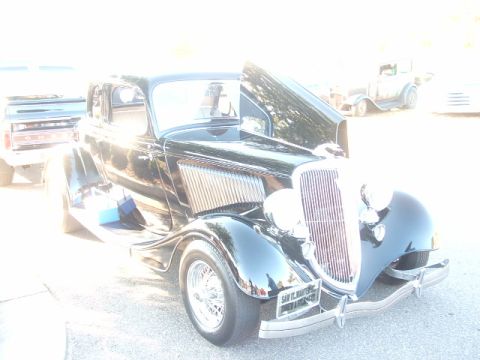 1971 Ford Ranchero - Black 1934 Ford Coupe, hood open, parked outdoors with other vehicles visible.