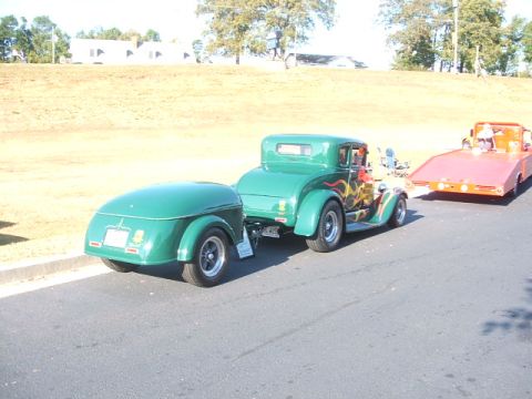 1971 Ford Ranchero - A green hot rod coupe tows a matching trailer, with a flatbed tow truck visible behind it.