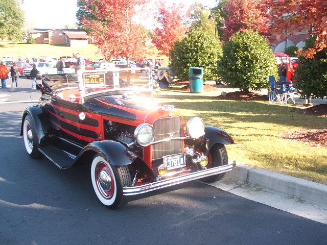 Black and red convertible hot rod with red racing stripes, white-wall tires, and a "FOR SALE" sign on the windshield