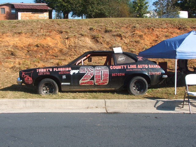 Black stock car with red number 20 on the side, advertising Tommy's Plumbing and County Line Auto Sales