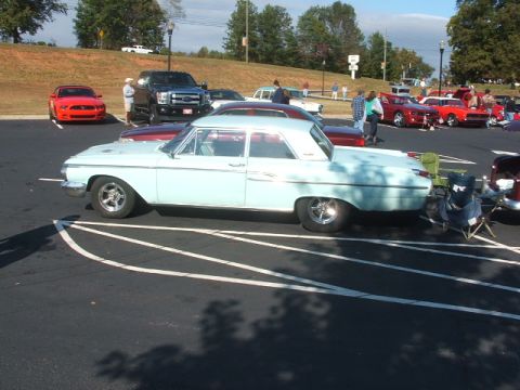 1971 Ford Ranchero - A light blue vintage sedan is parked in a lot with several other vehicles visible in the background.