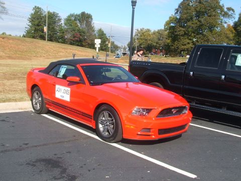 1971 Ford Ranchero - A bright orange convertible sports car is parked next to a black pickup truck in a parking lot.
