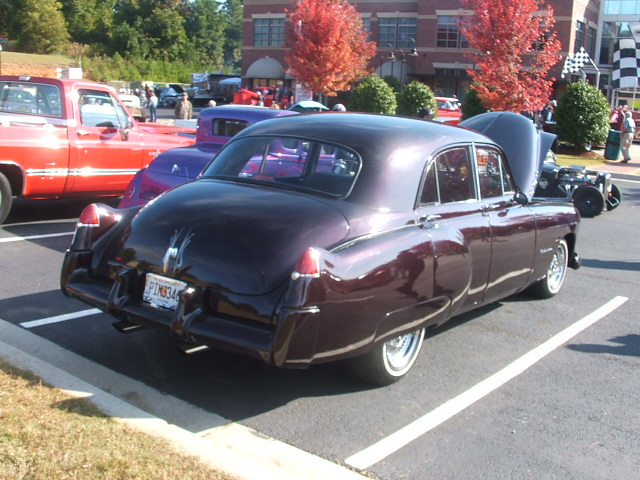 Dark purple sedan parked in a lot, rear view. License plate reads PIM334. Hood is open on a vehicle behind it