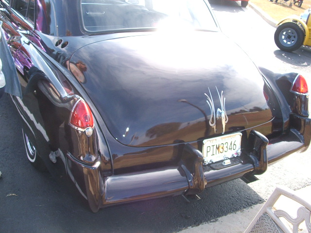 Rear view of a dark-colored classic car with pinstripes and a license plate reading PIM3346