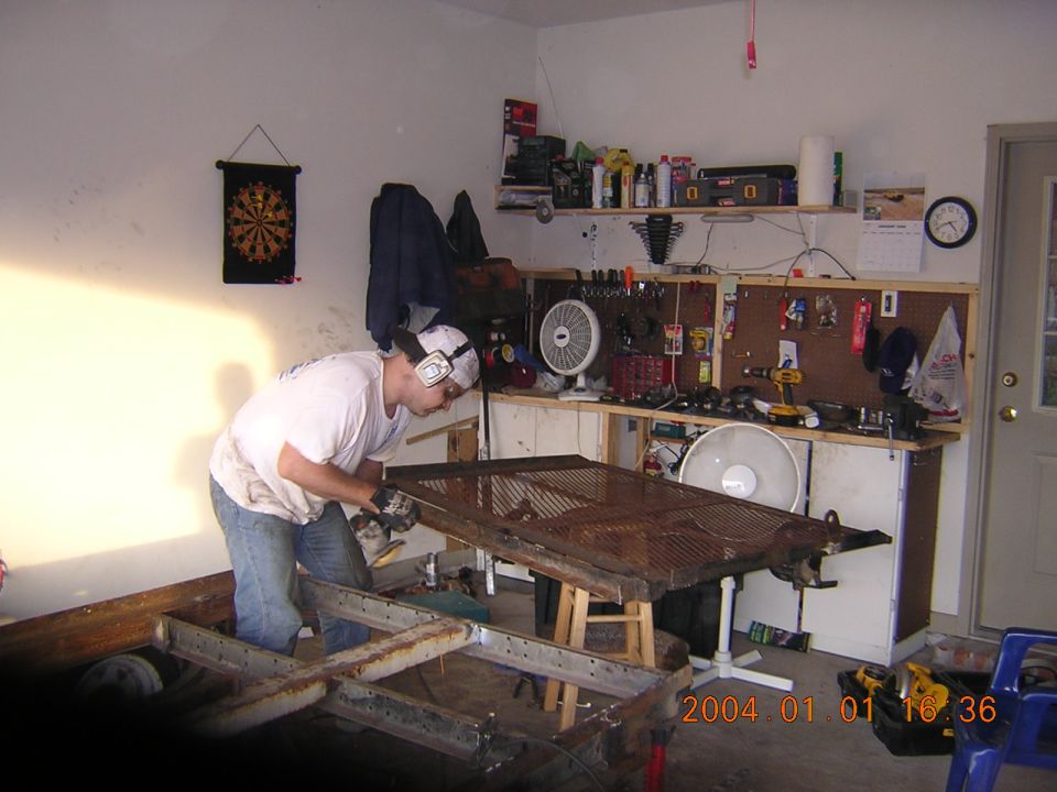 Man in garage grinding on a metal frame. Tools and fans on workbench behind him