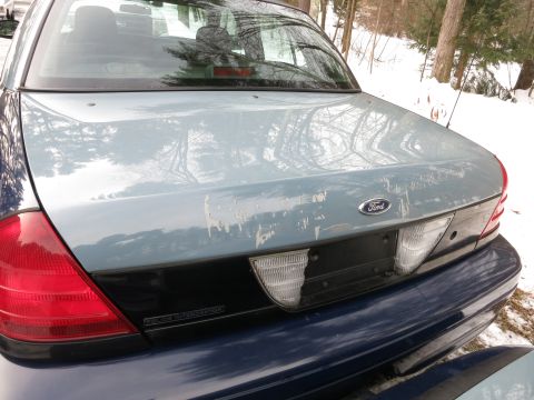 2001 Ford Crown Victoria - The rear of a 2001 Ford Crown Victoria shows peeling paint on the trunk lid and a 'Police Interceptor' badge.