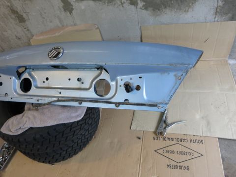 2001 Ford Crown Victoria - A light blue trunk lid, a Mercury emblem, is shown resting on a tire, likely awaiting repair or installation.