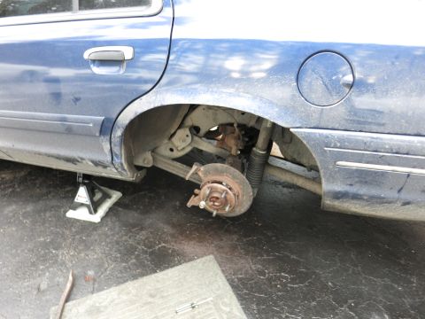 2001 Ford Crown Victoria - The rear wheel assembly of a blue 2001 Ford Crown Victoria is exposed, with the wheel removed and the car on a jack stand.