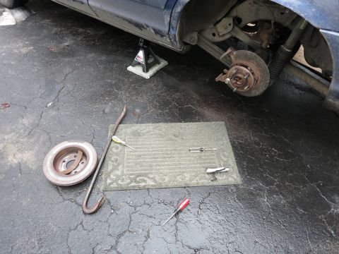 2001 Ford Crown Victoria - Tools and a removed brake rotor lie on the ground next to a car with its rear wheel assembly disassembled.