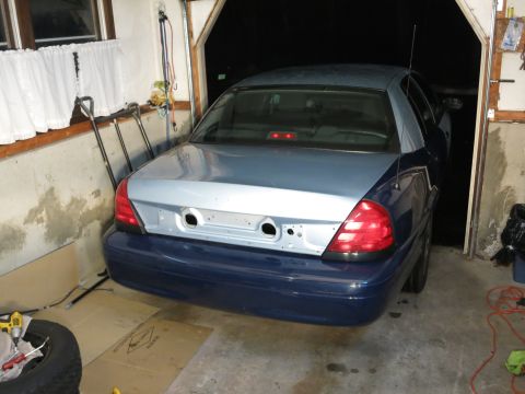 2001 Ford Crown Victoria - The rear of a 2001 Ford Crown Victoria, showing its blue lower body and silver trunk, is parked in a garage.