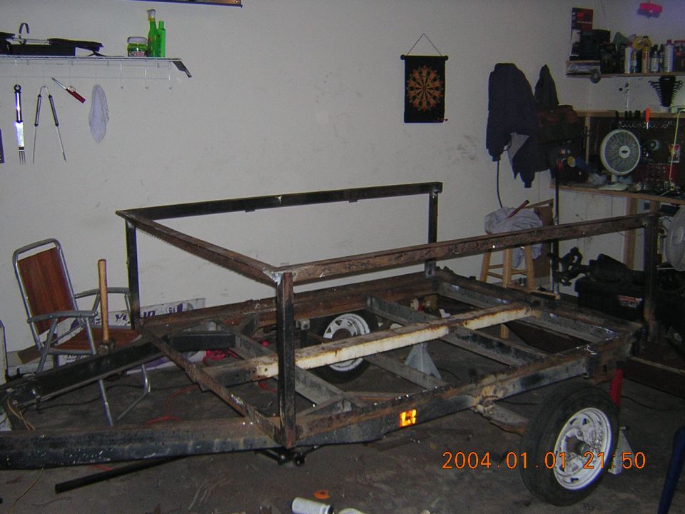 Trailer frame under construction in a garage, with metal tubing and wheels visible