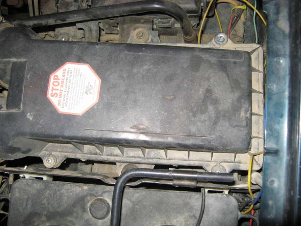 Engine air filter housing with a red and white 'STOP DO NOT DISCARD' sticker