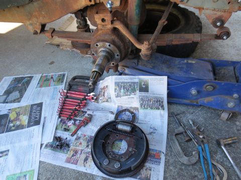 1946 Jeep Willys - A close-up view of a vehicle's front axle assembly and brake drum, surrounded by tools laid out on newspapers.