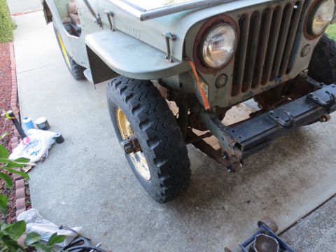 1946 Jeep Willys - Front view of a light green Jeep Willys with visible rust and a large tire with a yellow rim.