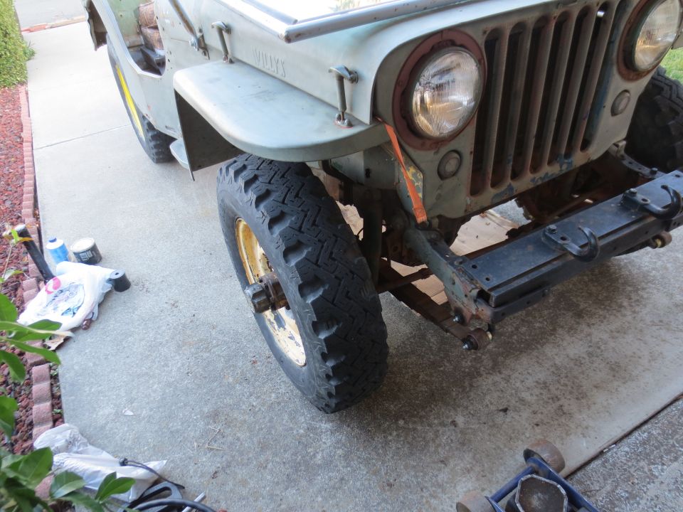 Light green Jeep Willys front end with rust on grille and bumper, showing a large tire and yellow rim