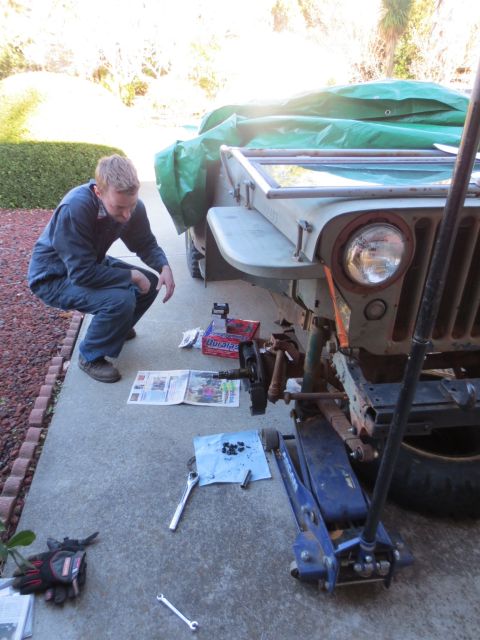 1946 Jeep Willys - A person works on the front wheel cylinder of a vintage Jeep, with tools and parts laid out on the driveway.