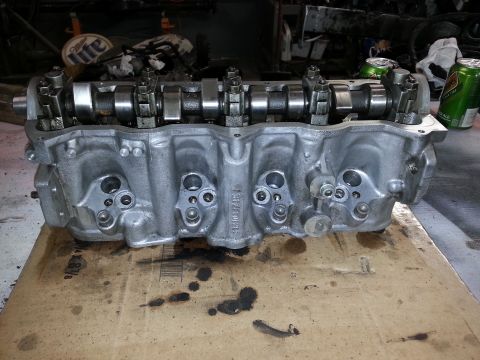 2002 Volkswagen Jetta - Engine cylinder head with camshafts and valves visible, resting on cardboard with oil stains.