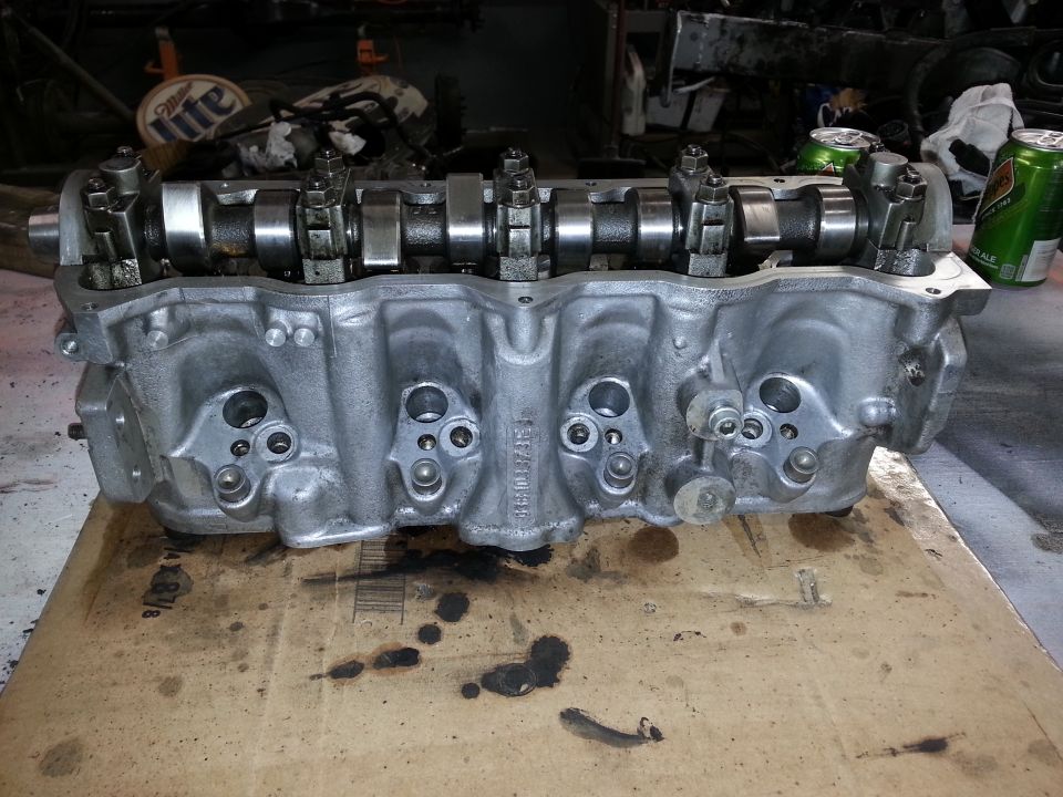 Engine cylinder head with camshafts and valves visible, resting on cardboard