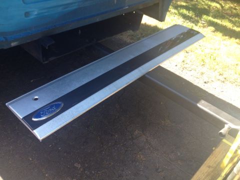 1993 Ford Bronco - A Ford tailgate trim piece is shown, detached from a vehicle. The trim has a blue oval Ford badge.
